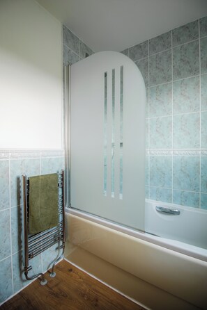 Een badkamer met een bad, een handdoekhouder en betegelde wanden.