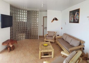 Un salon comprenant un canapé, des fauteuils, une table basse, un téléviseur et un élément décoratif mural.