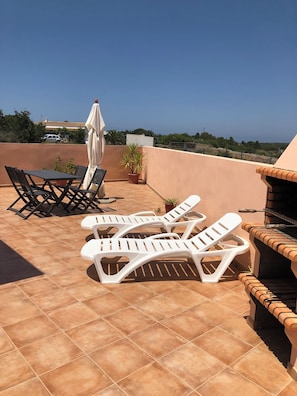 A rooftop terrace with a barbecue grill, lounge chairs, and a table with chairs.