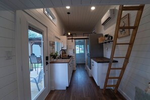 A narrow kitchen with white cabinets, a wooden countertop, and a ladder. - Less House, More Lake | Perfect for Couples (Kingston)