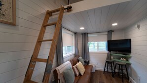 Un salón acogedor con una escalera de madera, un sofá de cuero marrón, un televisor y una zona de bar.