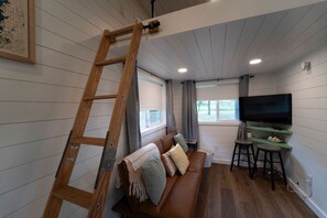 Un salon chaleureux avec une échelle en bois, un canapé en cuir marron, un téléviseur et un coin bar.