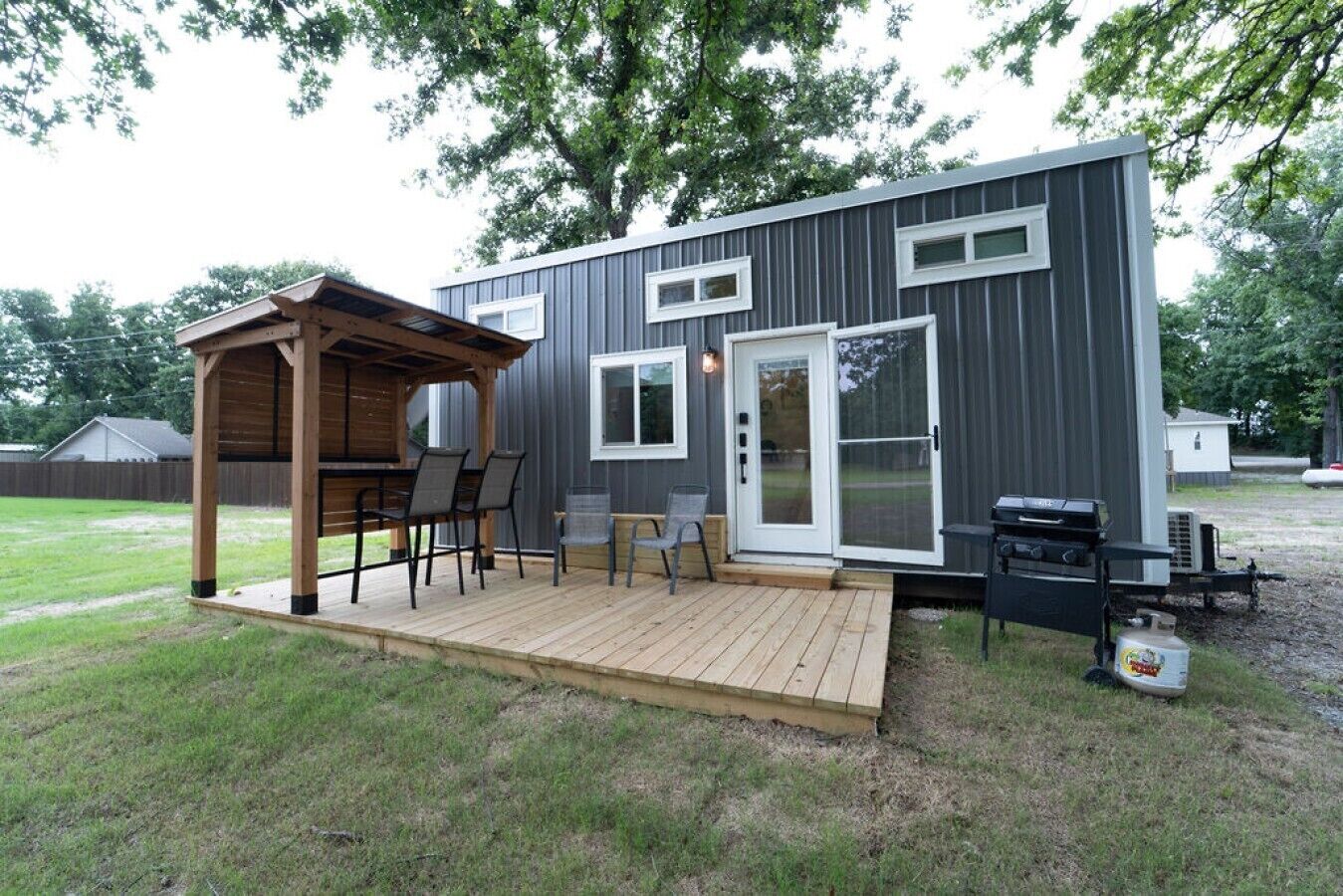 A compact, modern outdoor kitchen area with a wooden pergola, a barbecue grill, and a seating arrangement.. Less House, More Lake | Perfect for Couples
