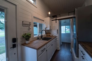 A kitchen with white cabinets, a wooden countertop, a black faucet, and a stainless steel refrigerator.
