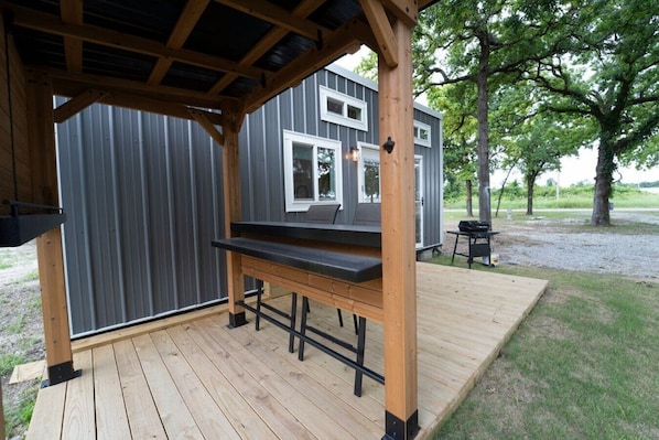 A covered outdoor area with a wooden bench and a grill.