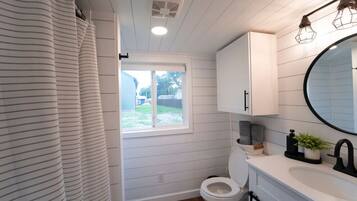 Ein Badezimmer mit Toilette, Fenster, Duschvorhang und Waschbecken mit Spiegel.