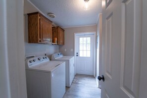 A laundry room with two washers and dryers, wooden cabinets, a white door, and a light fixture. - Big Lake, No Schedule | Sleeps 8 | Pet Friendly (Kingston)