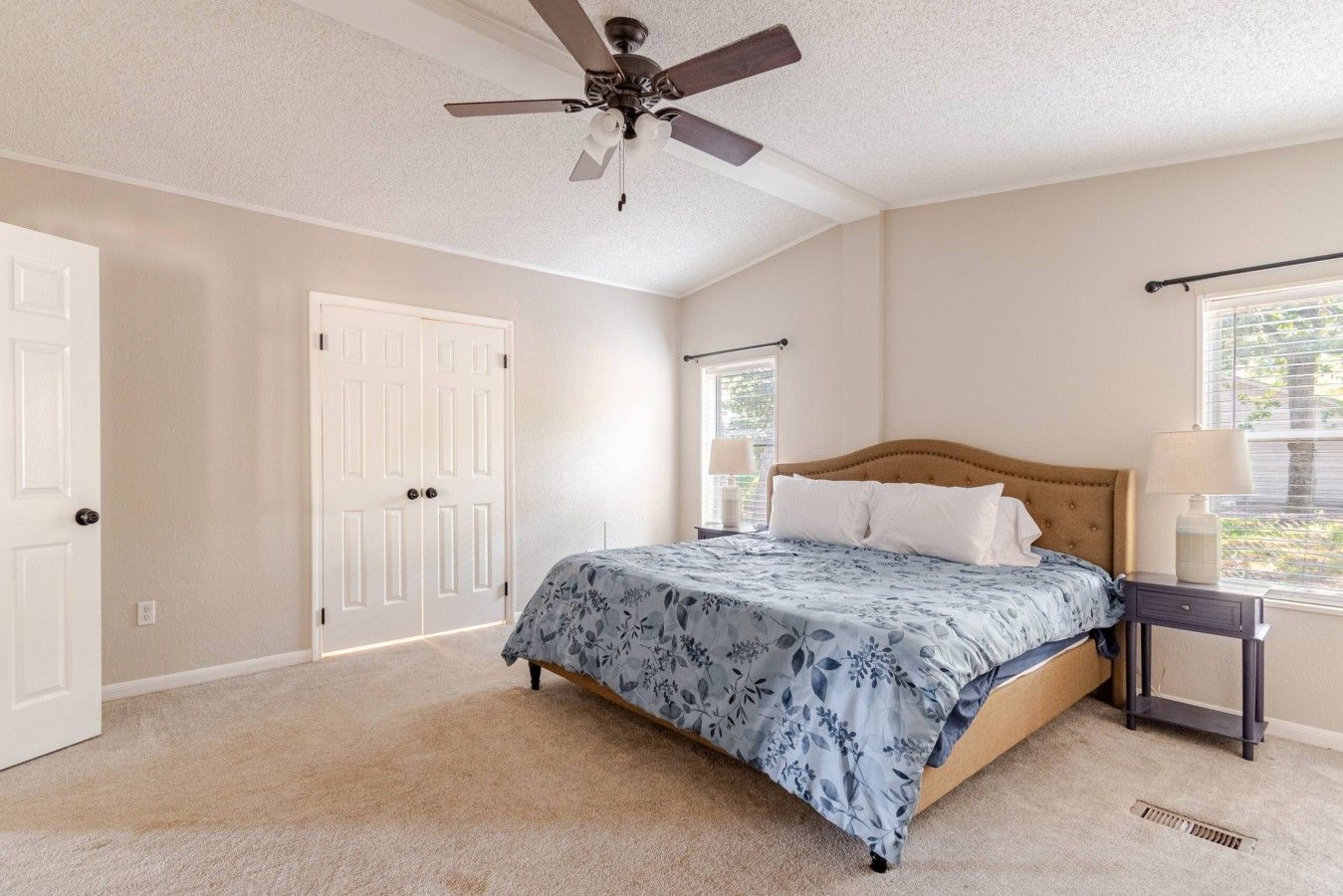 A bedroom with a bed, a ceiling fan, a window with blinds, and a door.