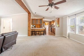 A spacious living area with a ceiling fan, a kitchen with wooden cabinets, and a large window providing natural light. - Big Lake, No Schedule | Sleeps 8 | Pet Friendly (Kingston)