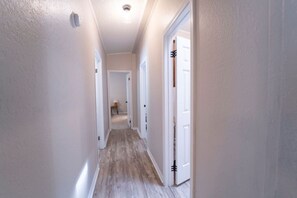 A narrow hallway with white walls and wooden flooring, leading to a door with a black handle. - Big Lake, No Schedule | Sleeps 8 | Pet Friendly (Kingston)