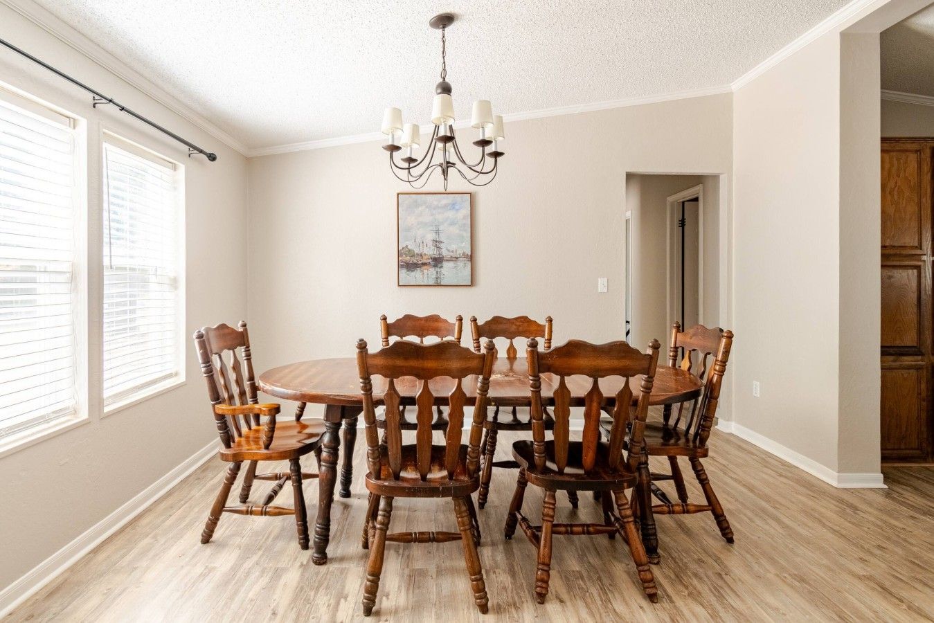 A dining room with a round table and six chairs, a chandelier, and a painting on the wall.