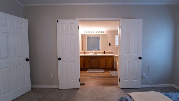 Een slaapkamer met een groot bed, een deur naar een badkamer met houten kasten en een spiegel.