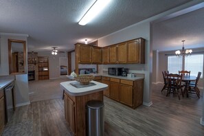 A modern kitchen with wooden cabinets, a central island, and a dining area with a chandelier. - Big Lake, No Schedule | Sleeps 8 | Pet Friendly (Kingston)