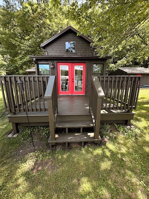 A wooden deck with a red door and a small porch. - Cozy Lakefront Cottage w/ Private Dock — All-Season Lake Escape (Delton)