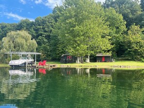 A lakeside cabin with a dock, a red chair, and a small shed.