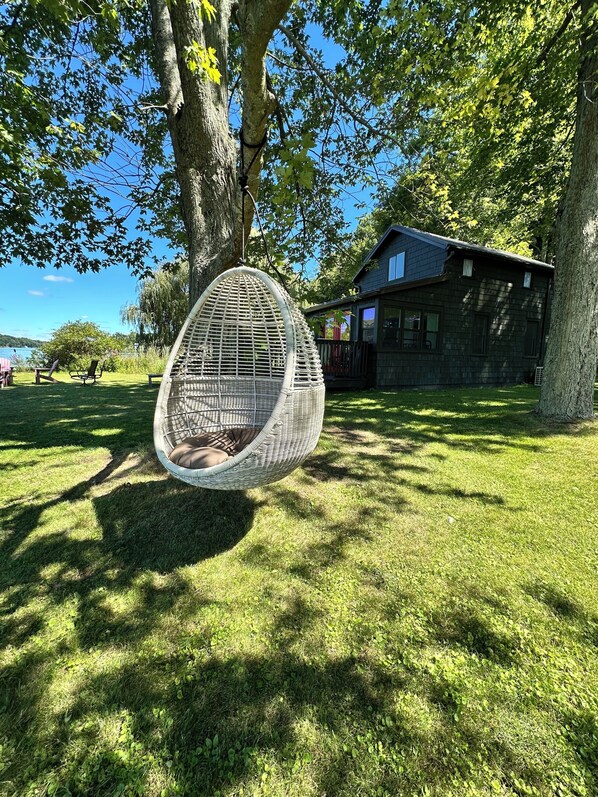 A hanging egg chair in a grassy area with a house in the background.