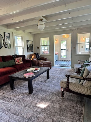 A living room with a red sofa, a brown leather chair, a coffee table, and a striped armchair. - Cozy Lakefront Cottage w/ Private Dock — All-Season Lake Escape (Delton)