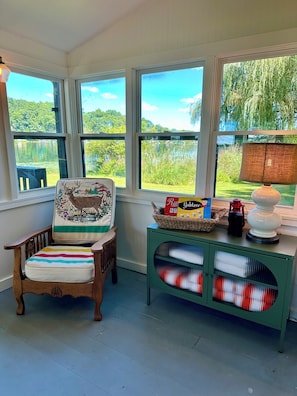 A room with a wooden chair, a green cabinet with glass doors, and large windows overlooking a lake. - Cozy Lakefront Cottage w/ Private Dock — All-Season Lake Escape (Delton)