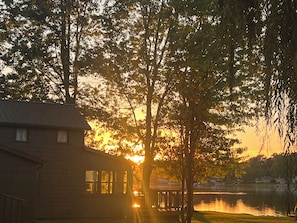 A lakeside cabin with a view of the sunset, surrounded by trees and a calm lake. - Cozy Lakefront Cottage w/ Private Dock — All-Season Lake Escape (Delton)