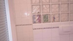 Een badkamer met toilet, wastafel en een betegelde muur met een raam boven de wastafel.