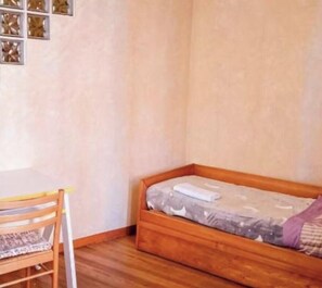 Ein kleines Zimmer mit einem hölzernen Bett, einem Stuhl und einem Tisch.