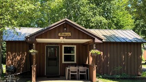 A wooden building with a sign reading 'AspenGlow,' a door, a window, and a small outdoor seating area with chairs.