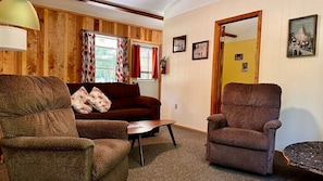 A cozy room with a brown sofa, two armchairs, a small table, and a door marked 'SKI'.