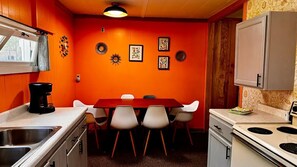 A kitchen with a red wall, white cabinets, a dining table with four chairs, a stove, and a coffee maker.