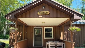 A wooden building with a sign reading 'AspenGlow,' a door, two tables with chairs, and hanging flower baskets.