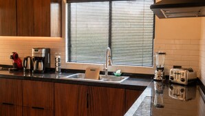 A modern kitchen with wooden cabinets, a black countertop, a window with blinds, and a toaster. - Family home with private pool, loft and garage, super central location! (La Paz)