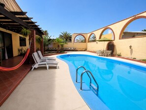 Ein Schwimmbecken mit Liegestühlen, einer Pergola und Bogenfenstern.