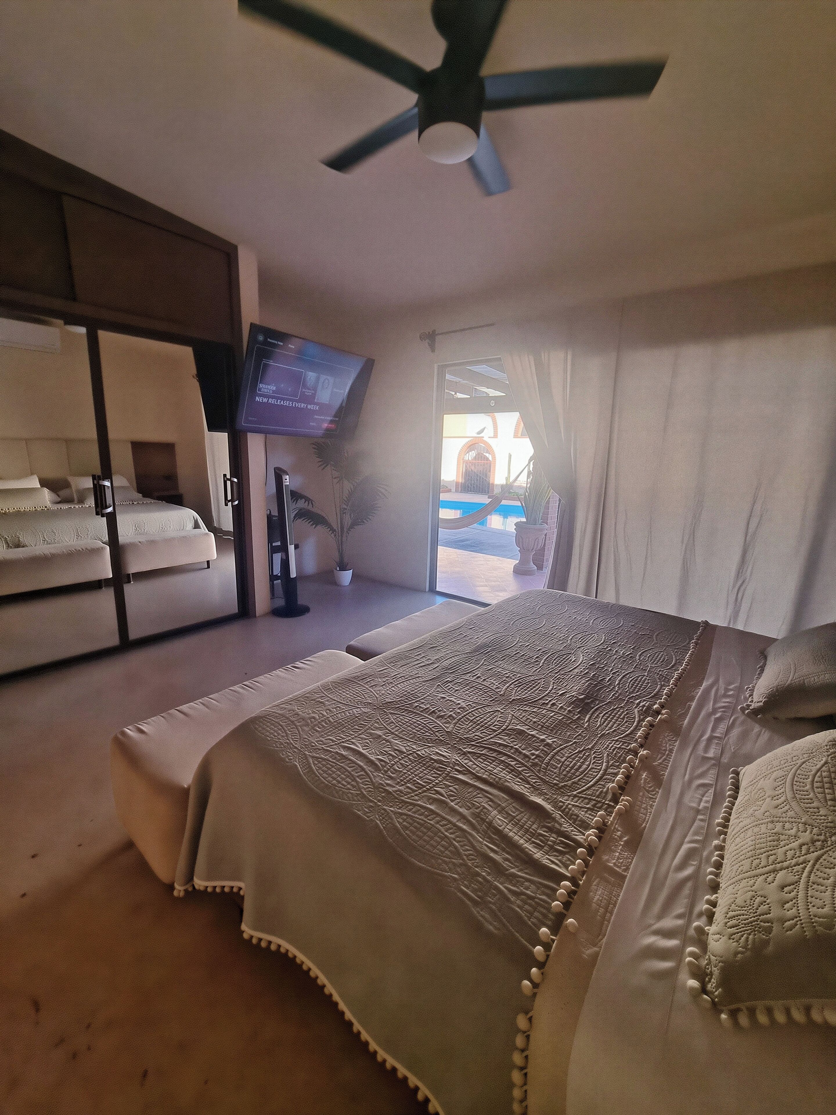 Een slaapkamer met een bed, een plafondventilator, een televisie en uitzicht op een zwembad.