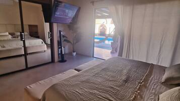 Een slaapkamer met een bed, een plafondventilator, een televisie en uitzicht op een zwembad.