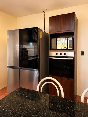 Eine Küche mit einem Edelstahl-Kühlschrank, einem eingebauten Backofen und einer Mikrowelle. Über dem Backofen befindet sich ein Holzschrank und die Arbeitsfläche ist schwarz.