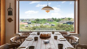 A dining area with a large window, a table set for four, and a view of houses in the distance. - "Nyyrikki" - 350m from the sea by Interhome (Ringkøbing)