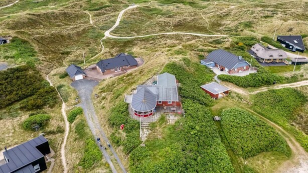 An aerial view of a coastal property with multiple buildings, including a large circular structure, surrounded by green vegetation and a winding road. - "Nyyrikki" - 350m from the sea by Interhome (Ringkøbing)