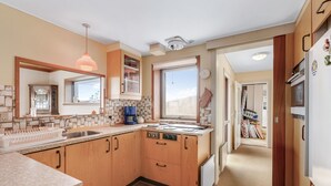 A compact kitchen with wooden cabinets, a built-in stove, a coffee maker, and a window providing natural light. - "Nyyrikki" - 350m from the sea by Interhome (Ringkøbing)