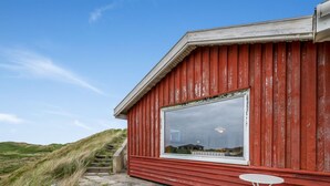 A red building with a large window, a wooden deck, and a green chair. - "Nyyrikki" - 350m from the sea by Interhome (Ringkøbing)