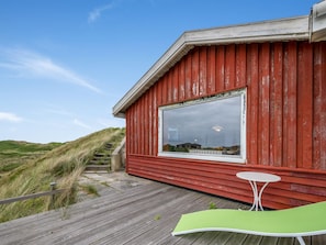 Ein rotes Gebäude mit einem großen Fenster, einer Holzterrasse und einem grünen Stuhl.