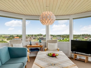 Ein Zimmer mit großem Fenster, Fernseher, Obst auf einem Tisch und einer Lampe.