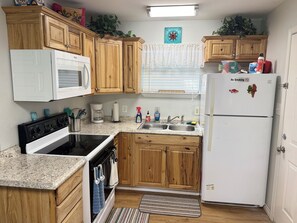 A compact kitchen with wooden cabinets, a white refrigerator, a stove, and a sink. - Emma's Casa Bonita; Cozy Coastal Cottage Near Rockport Attractions (Rockport)
