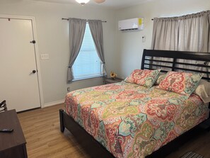 A bedroom with a bed, a window with curtains, an air conditioning unit, and a door. - Emma's Casa Bonita; Cozy Coastal Cottage Near Rockport Attractions (Rockport)