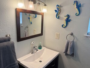 A bathroom with a sink, mirror, and decorative seahorse wall art. - Emma's Casa Bonita; Cozy Coastal Cottage Near Rockport Attractions (Rockport)
