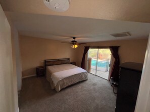 Una camera da letto con un letto, una ventola a soffitto, una porta scorrevole in vetro che dà su una piscina e un comò.