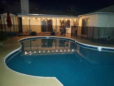 A swimming pool with a curved edge, surrounded by a covered patio area with string lights.. 4-BEDROOM SPACIOUS HOME WITH A POOL, PERFECT FOR A FUN/RELAXING TIME IN ARIZONA