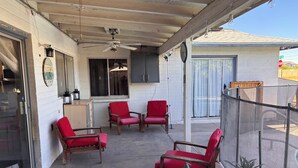 Ein überdachter Patio-Bereich mit Holzbänken, einem Tisch, einem Deckenventilator und einem Blumentopf.