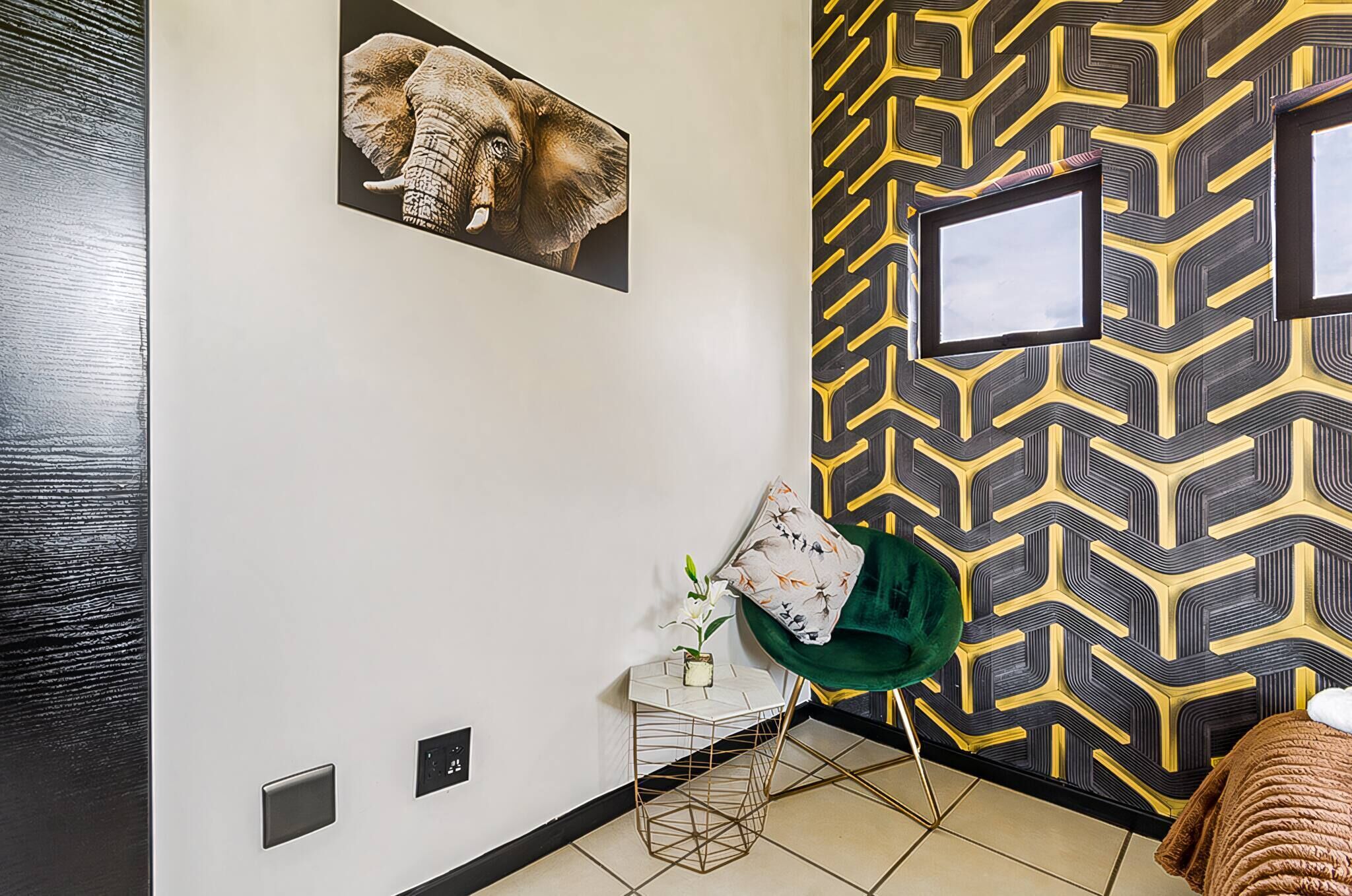 Una habitación con pared de diseño, un cuadro enmarcado de un elefante, una silla verde y una pequeña mesa con un florero.