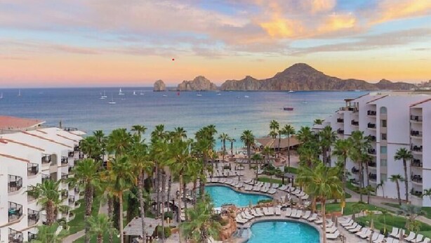 Ein Resort mit Pool, Palmen und Blick auf das Meer bei Sonnenuntergang.