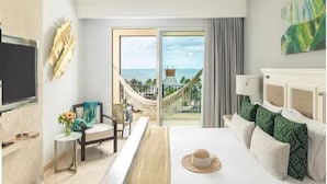 Ein Hotelzimmer mit einem großen Bett, einem Schreibtisch, einem Stuhl, einem Fernseher und Meerblick durch eine Schiebetür.