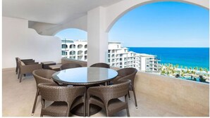Ein runder Tisch mit Korbstühlen auf einem Balkon mit Blick auf Strand und Meer.